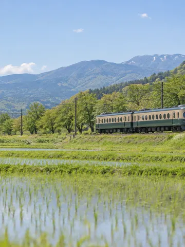 新緑の田園を走る丸窓の古い電車
