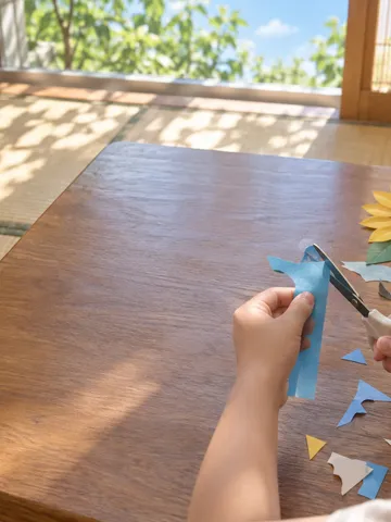 夏の昼間に子どもの手が紙をはさみで切る工作の様子