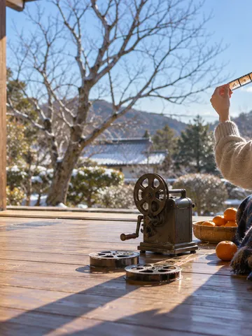 冬の縁側で映写機とフィルムを光にかざす手元