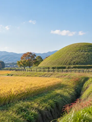 青空の下、草に覆われた古墳の丸い墳丘と小道