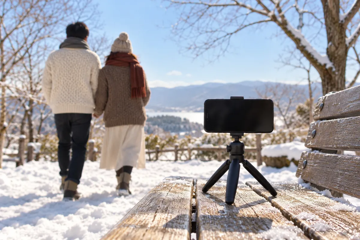 雪の公園のベンチでスマホを立て、ふたりが写真を撮る