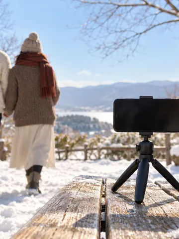 雪の公園のベンチでスマホを立て、ふたりが写真を撮る
