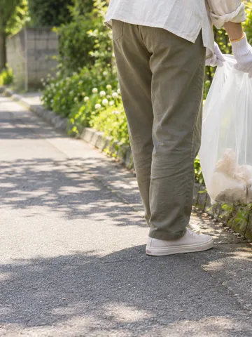 軍手でごみ袋を持ち道端のごみを拾う手元