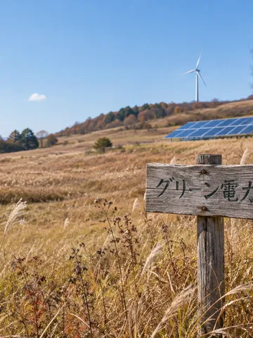 青空の下の太陽光パネルと風車、グリーン電力の木札