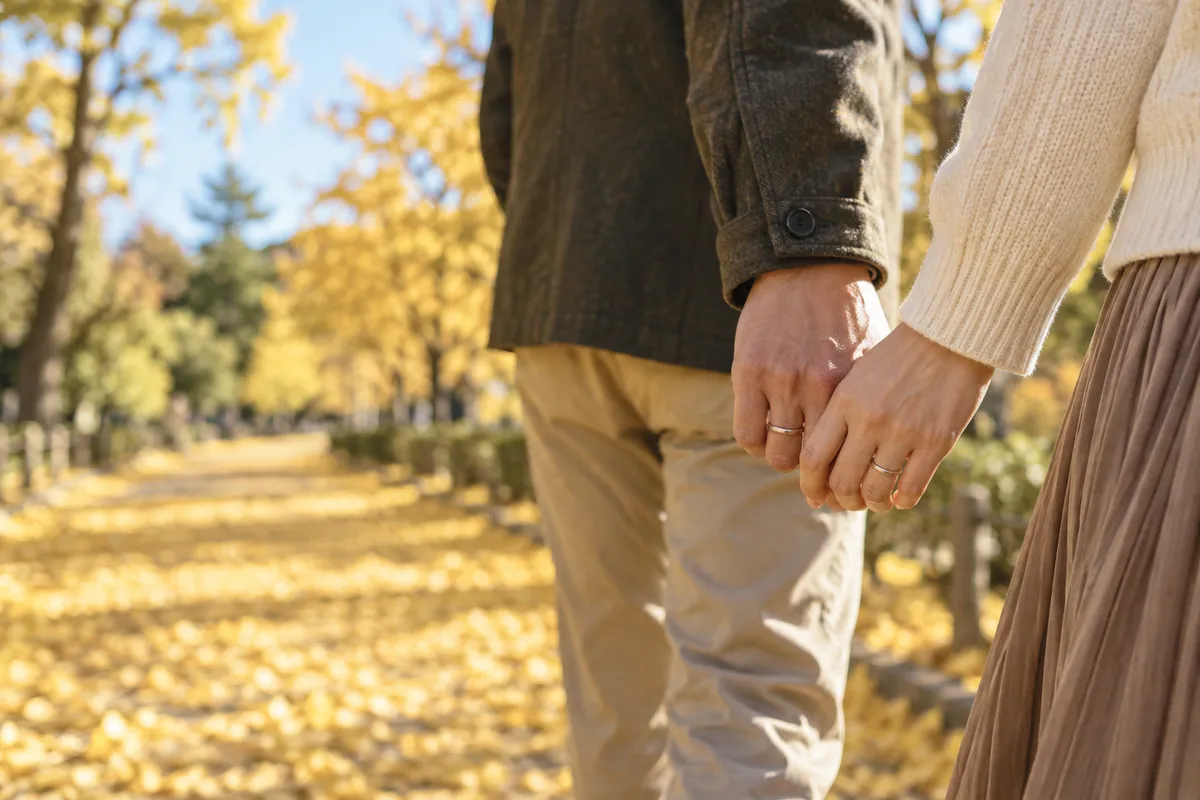 紅葉の道で手をつなぐふたりと、手元の指輪