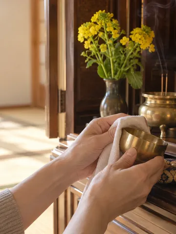 仏壇の仏具を布でふく手元と菜の花