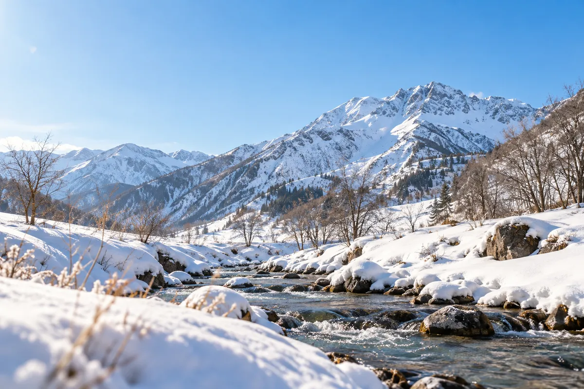 晴れた空の下、雪の山並みと手前を流れる小川
