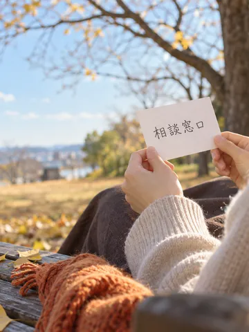 日なたのベンチで「相談窓口」と書かれたメモを持つ手元