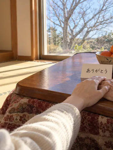 こたつの上で重ねた手とみかん、ありがとうのメモ