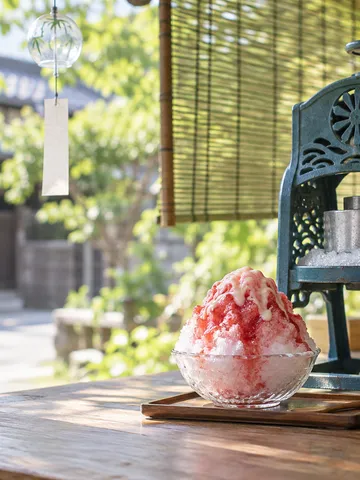 甘味処の店先で氷を削るかき氷器と、シロップのかかったかき氷