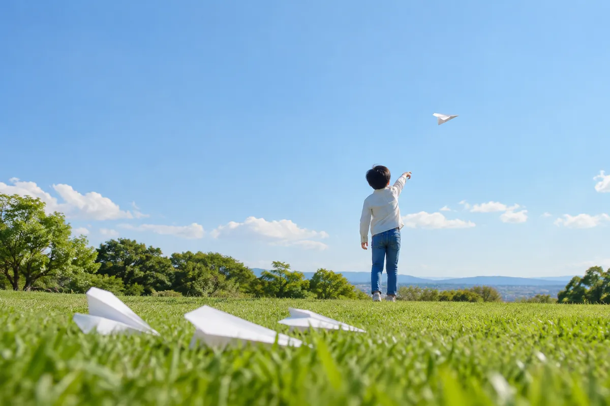 青空へ紙飛行機を飛ばす後ろ姿と芝生の紙飛行機