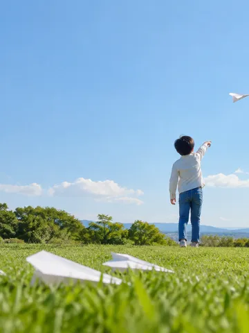 青空へ紙飛行機を飛ばす後ろ姿と芝生の紙飛行機