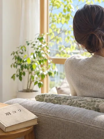肩に手を添えて休む後ろ姿と本、湯気の立つお茶