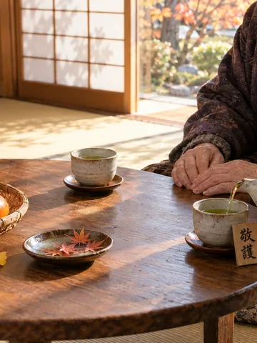 高齢者の手にお茶を注ぐ手と「敬護」の木札