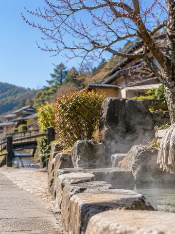 晴れた日の温泉街の道と湯気の立つ足湯