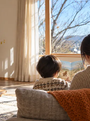 ソファで絵本を一緒に読む親子の後ろ姿