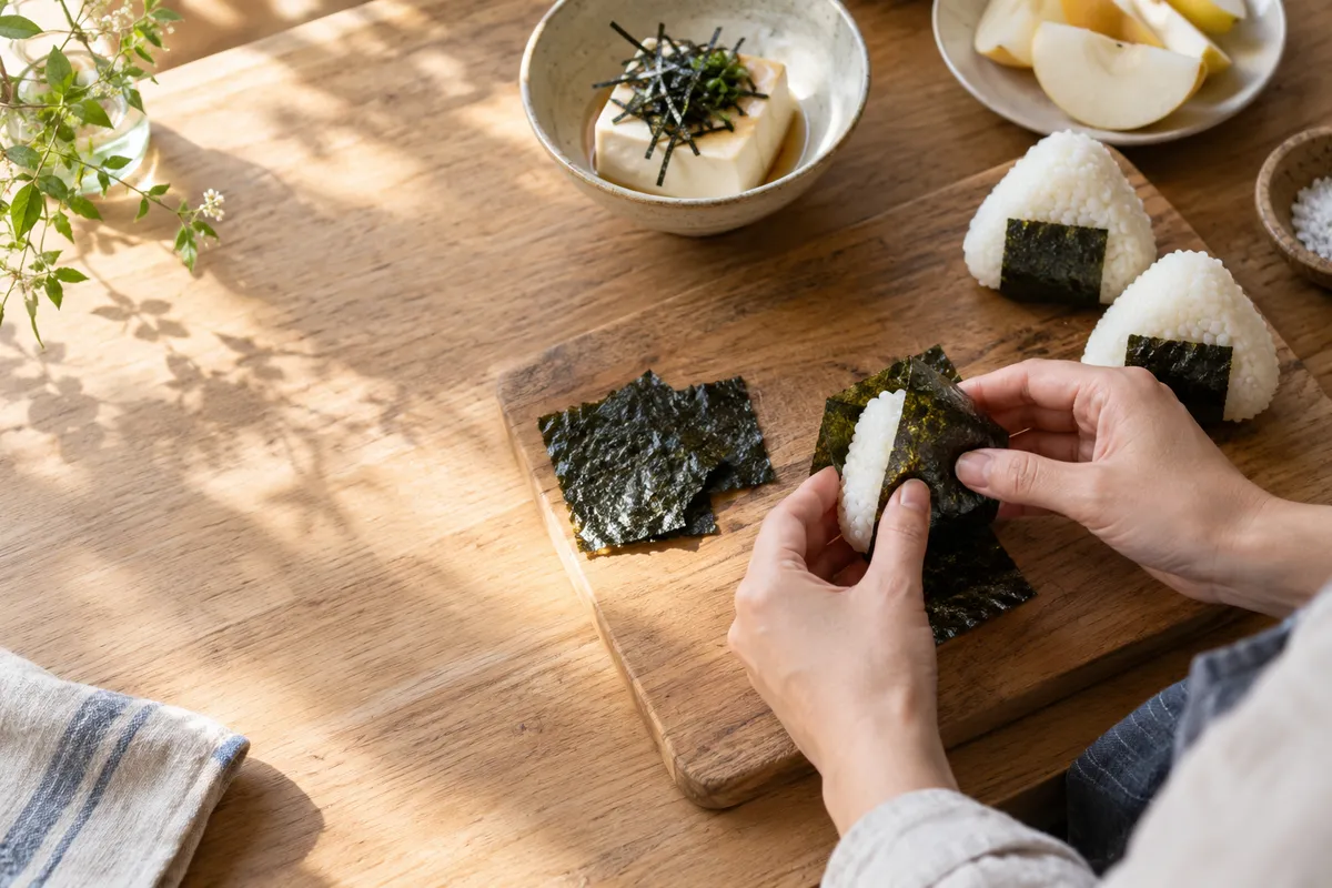 黒い海苔でおにぎりを包む手元と台所の食卓