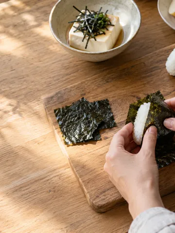 黒い海苔でおにぎりを包む手元と台所の食卓