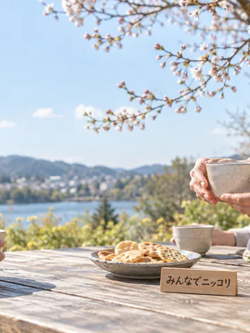 春の公園で湯のみを囲む人々の手元と木の札