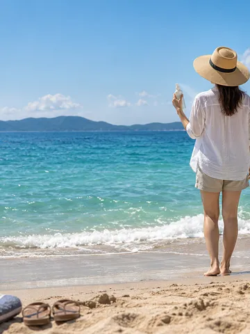 夏の砂浜で帽子をかぶった人の後ろ姿と無地のスプレー容器