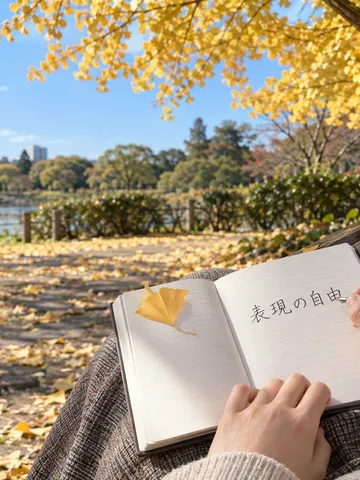 銀杏の下のベンチでノートに文字を書く手元