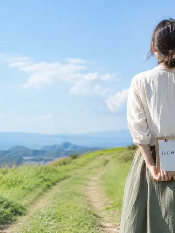 丘の小道の始まりで「はじめの一歩」と書いたメモを持つ後ろ姿