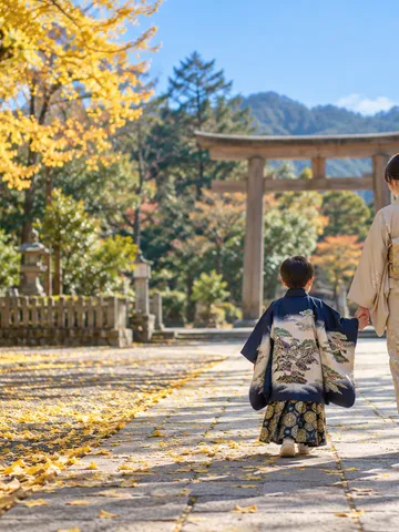 紅葉の境内を手をつないで歩く着物姿の子どもの後ろ姿
