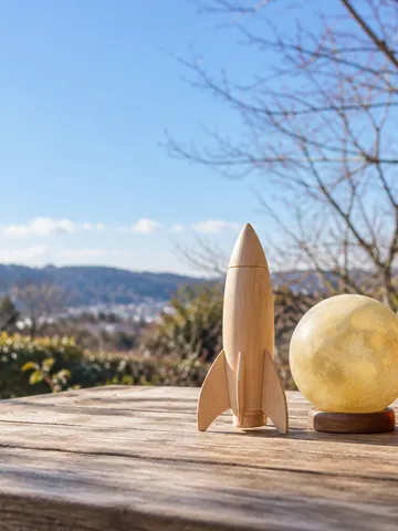 日なたの卓上に置かれた木製のロケット模型と月の飾り