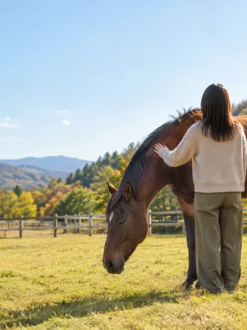 秋空の下、牧場で馬の首すじにそっと手を添ける後ろ姿