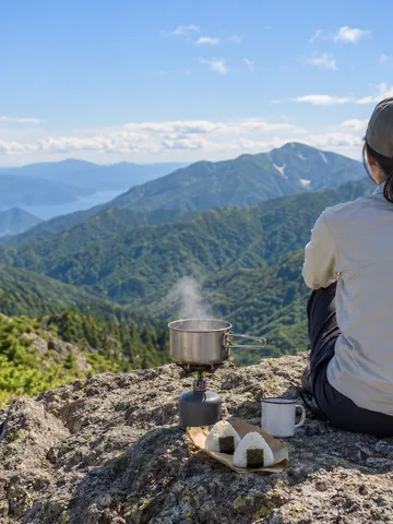 山頂の岩場で湯気の立つ鍋とおにぎりを並べた山ごはん