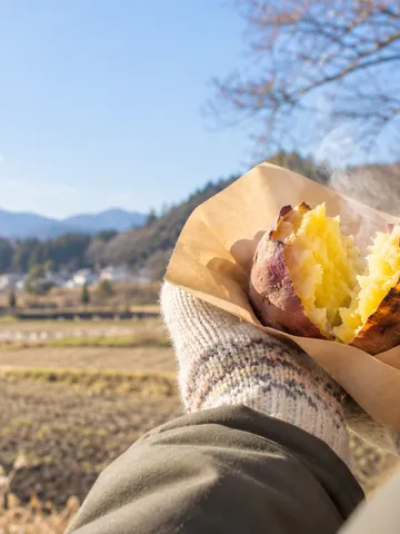 日なたで割った湯気の立つ焼き芋を持つ手元