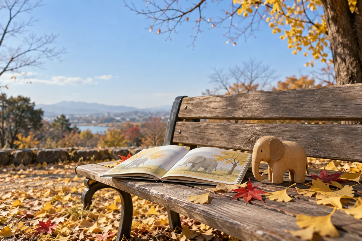 紅葉の落ち葉の公園のベンチに置かれたゾウの木のおもちゃと絵本